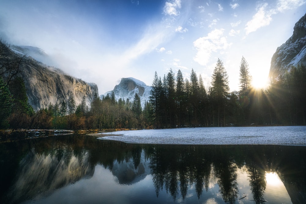 a lake surrounded by trees and mountains under a blue sky