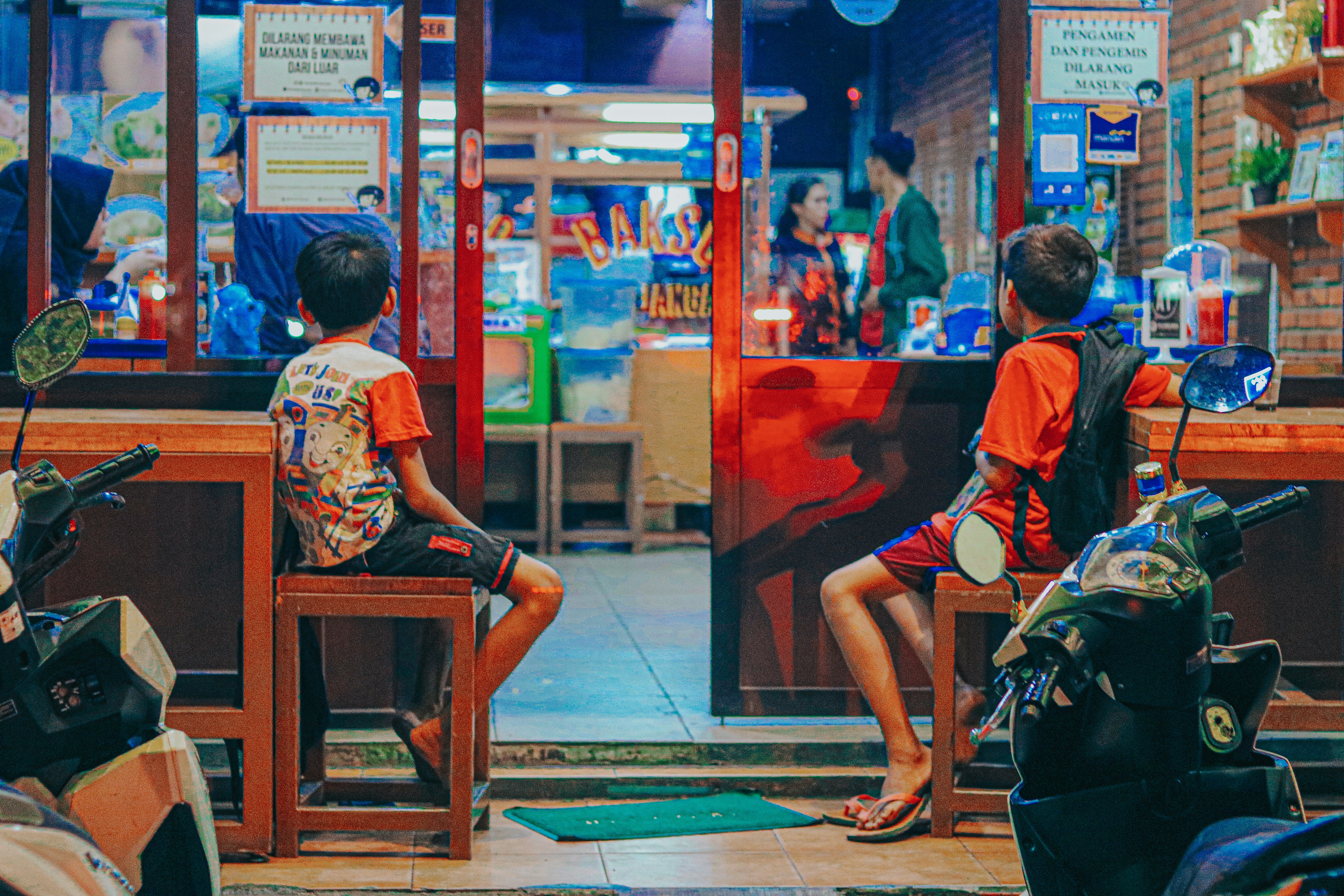 a couple of kids sitting on a bench in front of a store