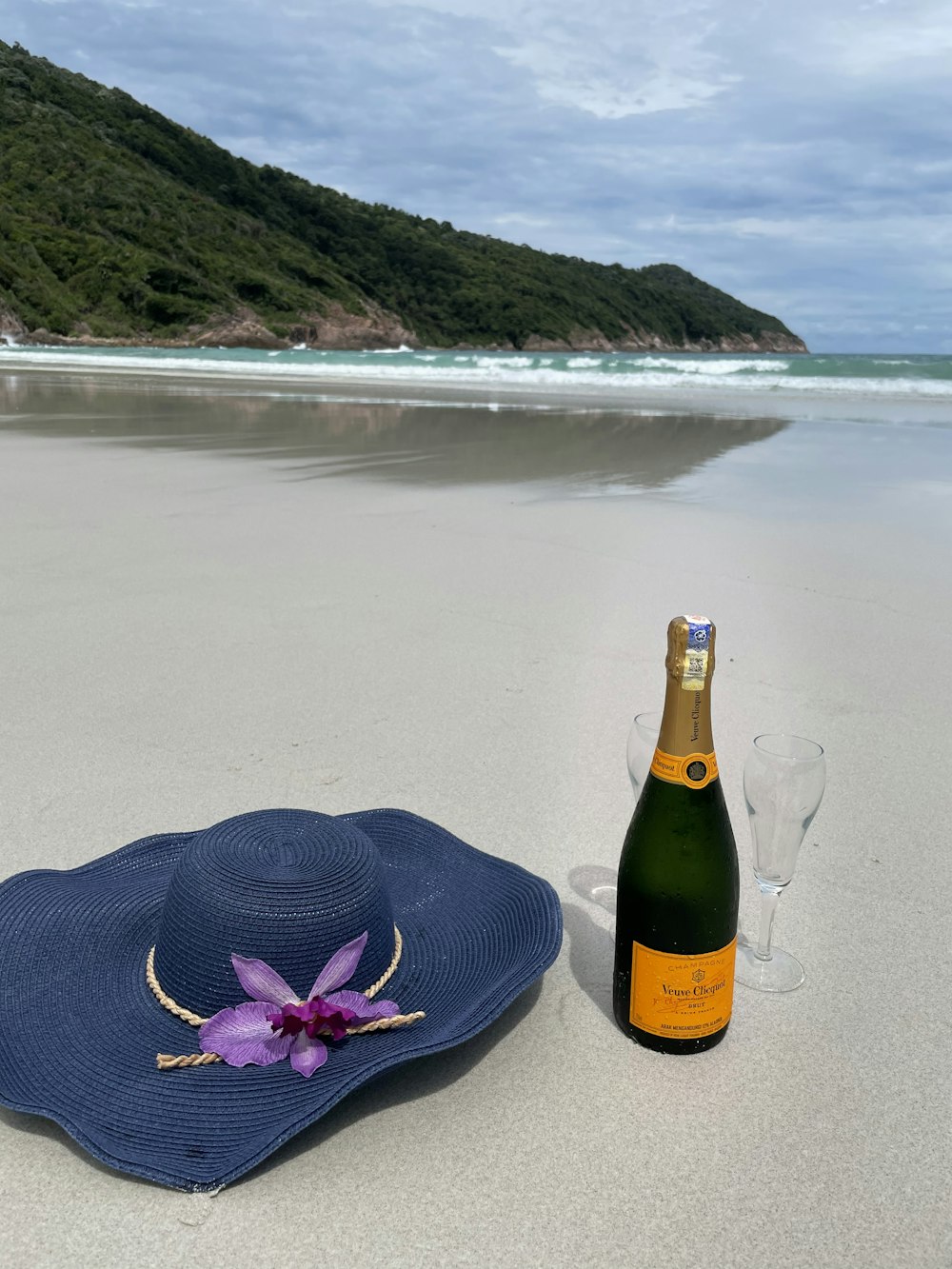 a bottle of wine and a hat on a beach