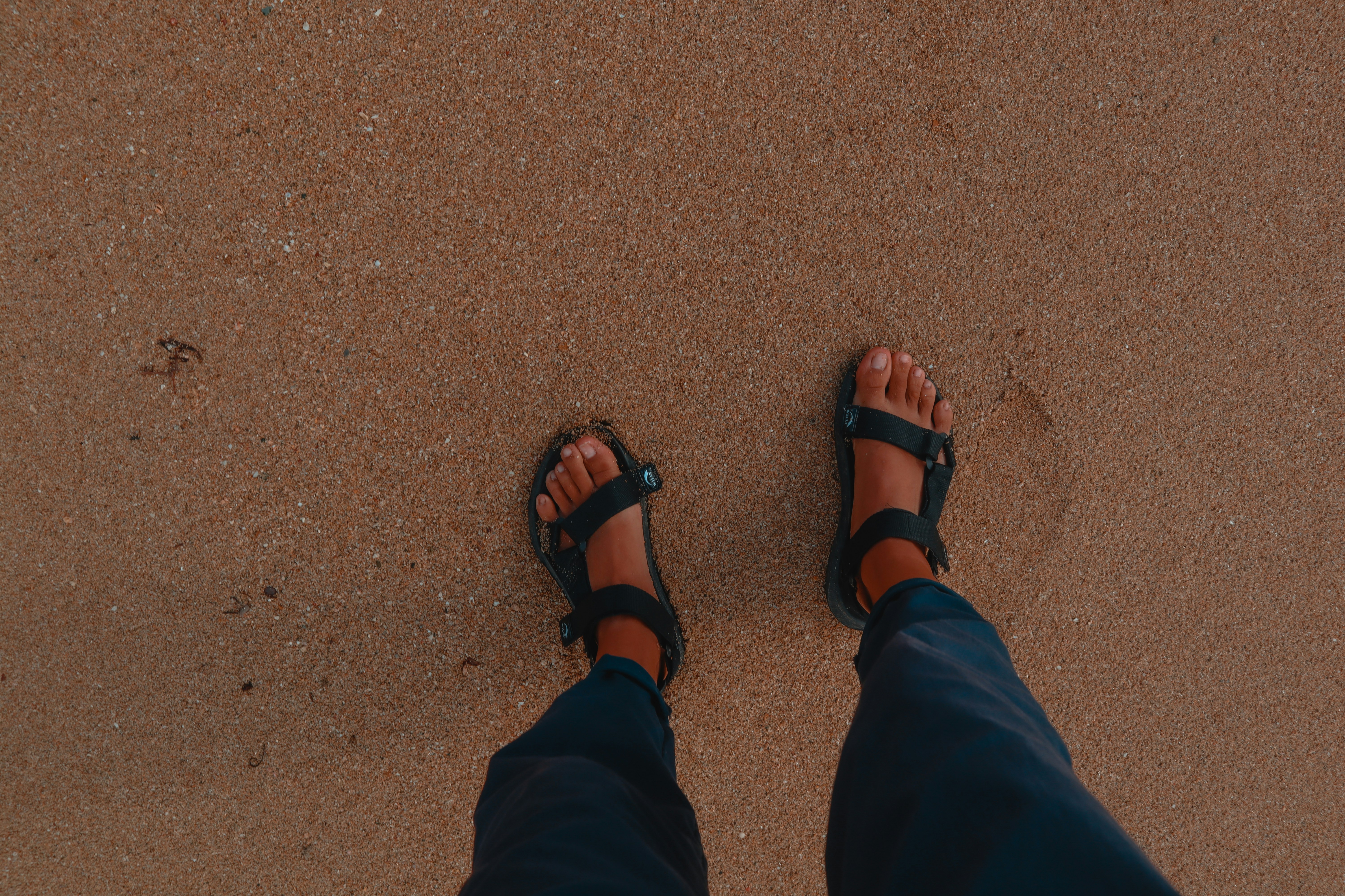 A woman's feet in sandals on a sandy beach with waves washing ashore.