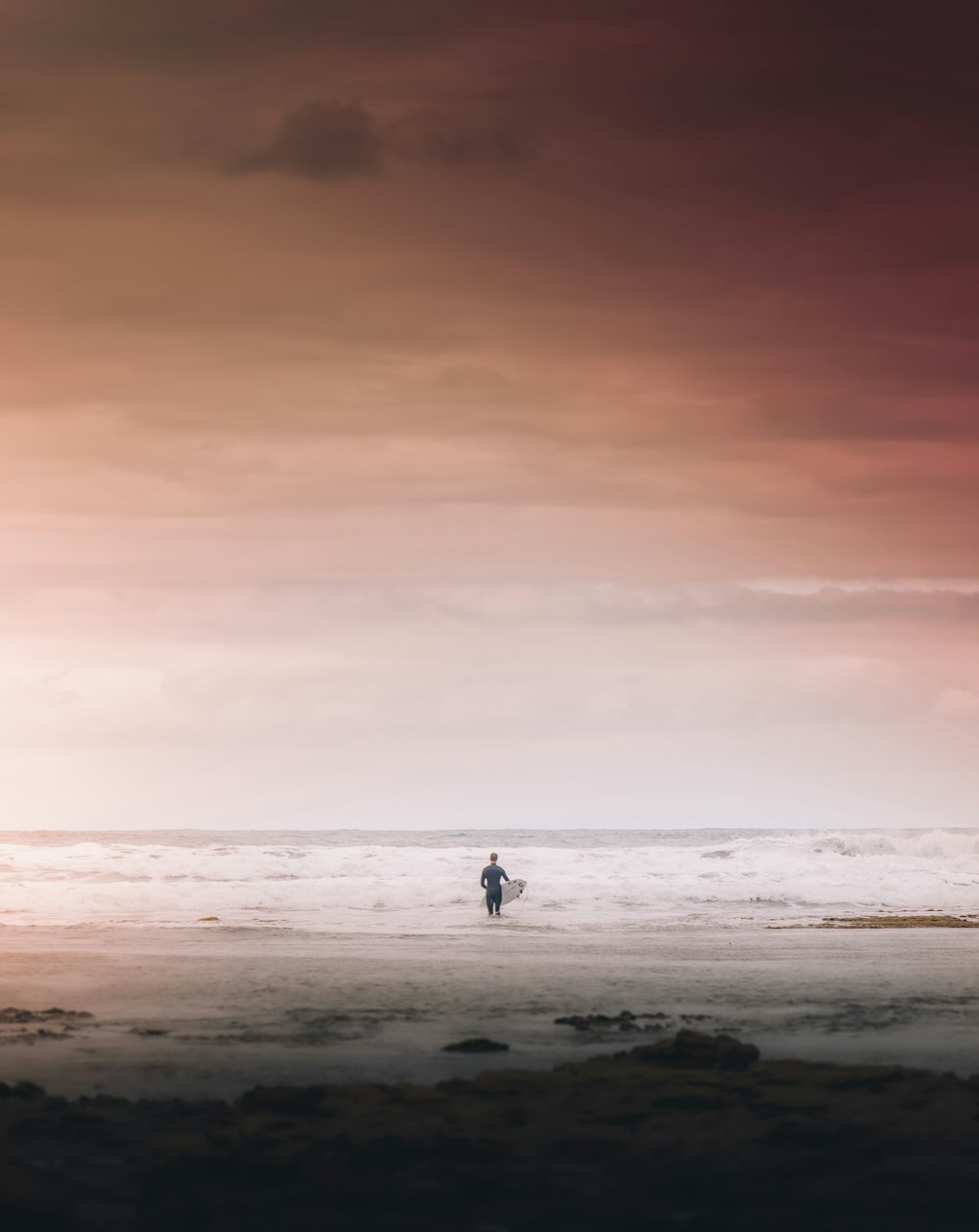 a person standing on a beach with a surfboard under a cloudy sky