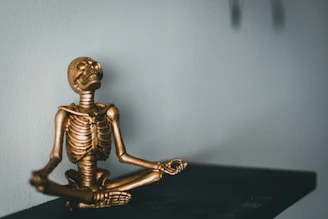 a golden skeleton sitting in a yoga position