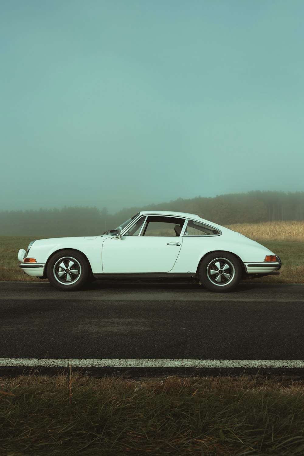 a white car driving down a road next to a field