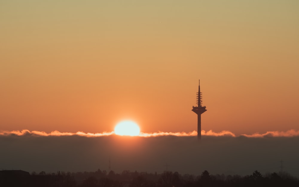 the sun is setting behind a tower in the sky