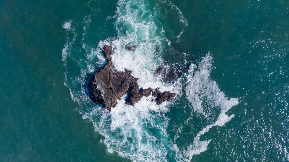 an aerial view of the ocean with a rock in the middle