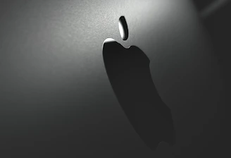 A close-up view of a metallic surface with a prominent, illuminated logo. The lighting creates a sleek and modern aesthetic with the logo casting a subtle shadow.