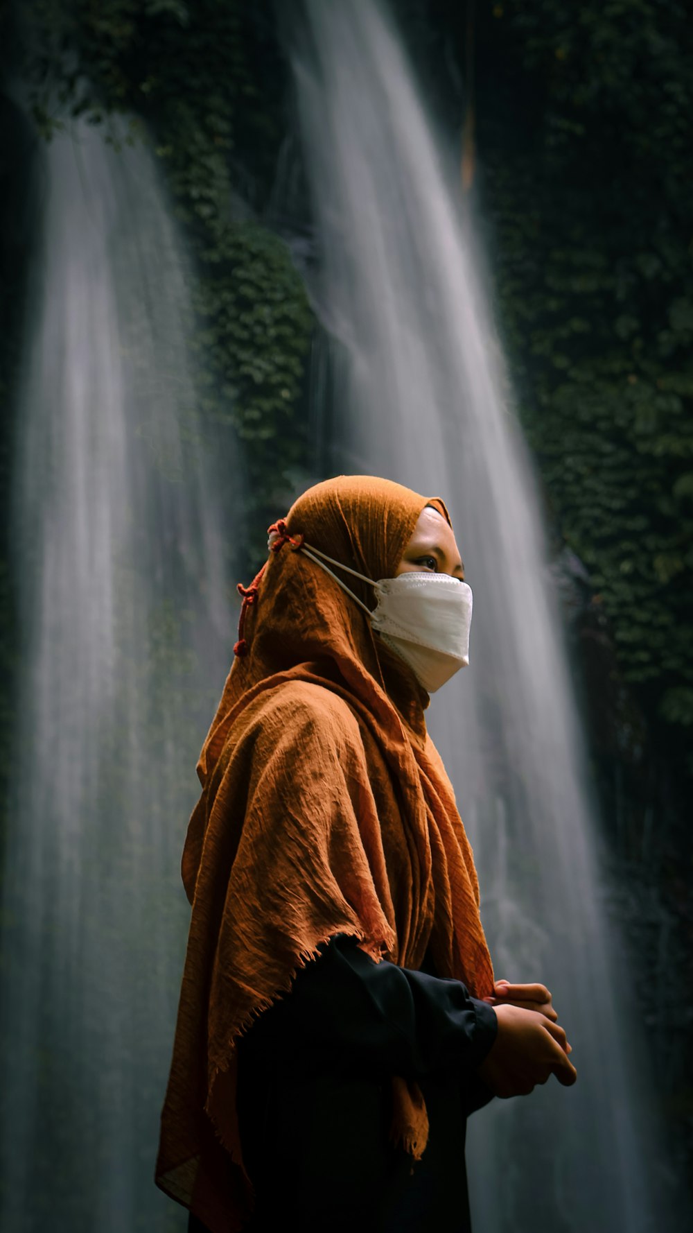 a person wearing a face mask standing in front of a waterfall