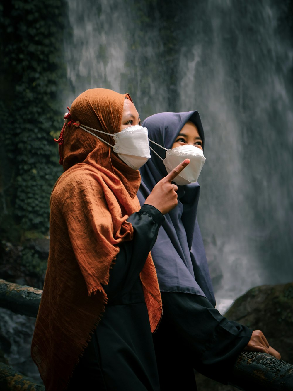 two women wearing masks standing in front of a waterfall