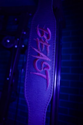 A leather strap with the word 'BEAST' embroidered in bold red letters. The background features a dimly lit gym setup with brick patterns visible on the wall.