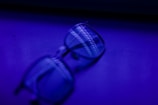 A pair of eyeglasses resting on a surface with a deep blue and purple lighting effect, creating a blur and shadow across the lenses.