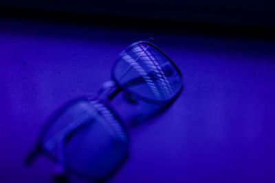 A pair of eyeglasses resting on a surface with a deep blue and purple lighting effect, creating a blur and shadow across the lenses.