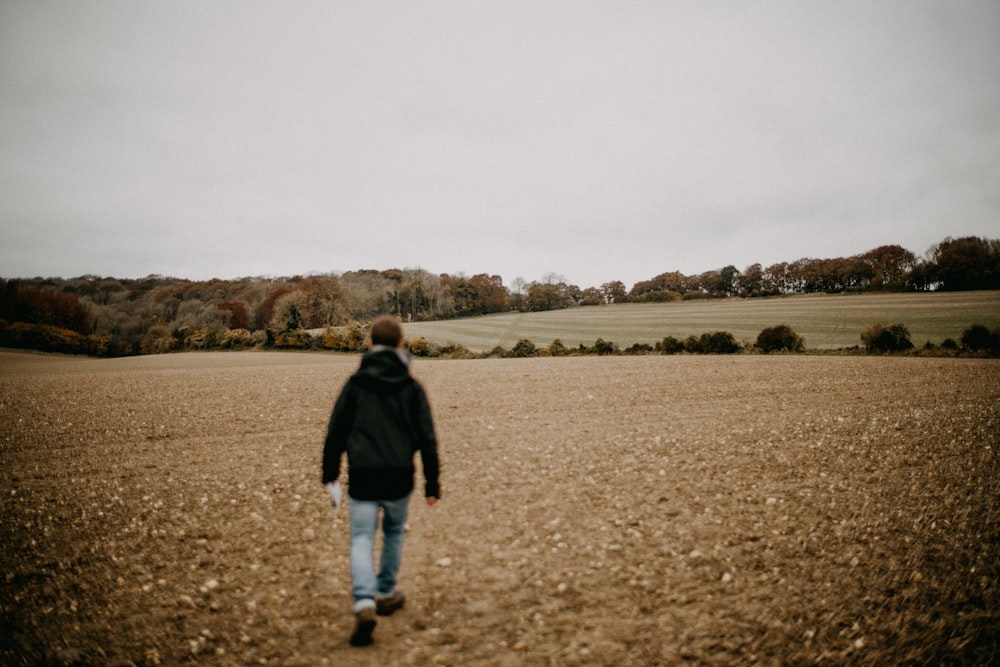 a man in a black jacket walking across a field