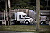 a semi truck driving down a street next to a wooden fence