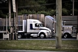 a semi truck driving down a street next to a wooden fence
