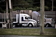 a semi truck driving down a street next to a wooden fence