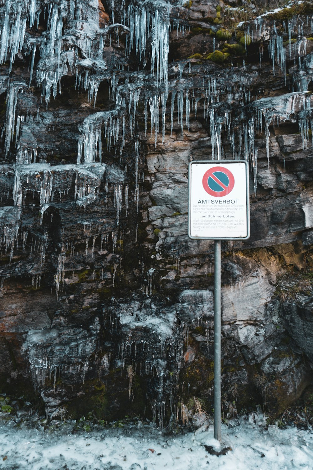 a sign on a pole in front of a wall of ice