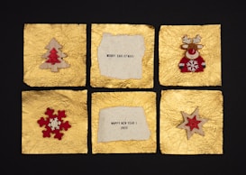 Six square panels with a textured golden background. The top left panel displays a wooden Christmas tree with a red center. The top middle panel contains a message: 'Merry Christmas!' on a torn piece of light paper. The top right panel features a red reindeer with decorative antlers. The lower left has a red snowflake with a smaller white snowflake at its center. The lower middle displays a message: 'Happy New Year 2022' on a similar torn piece of paper. The lower right panel has a wooden star with a red center.