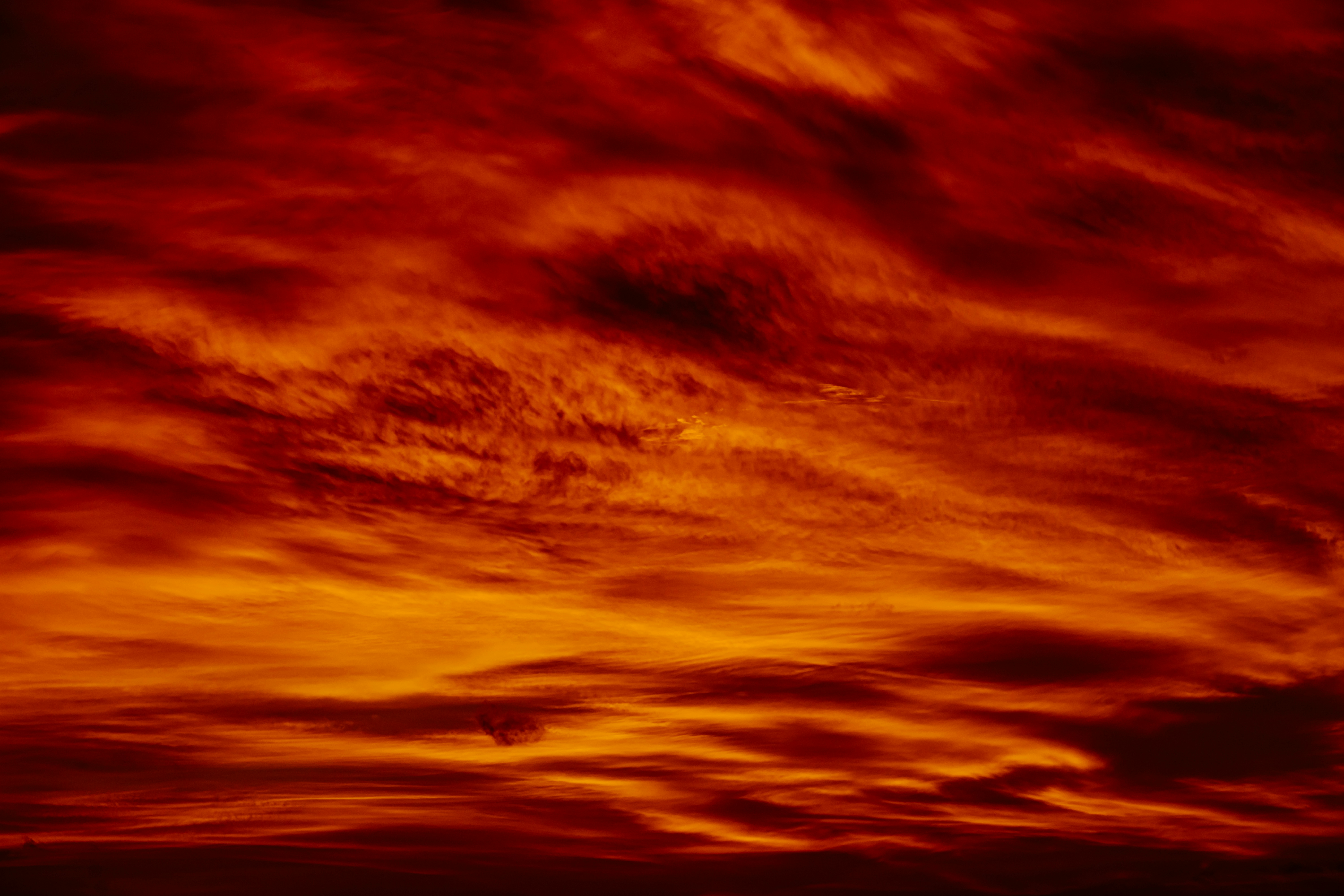 a red sky with clouds and a plane in the distance