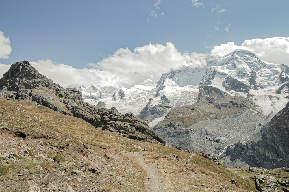 Ein Pfad, der einen Berg hinaufführt, mit schneebedeckten Bergen im Hintergrund