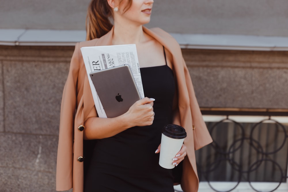 Eine Frau im schwarzen Kleid hält eine Kaffeetasse und ein Buch in der Hand