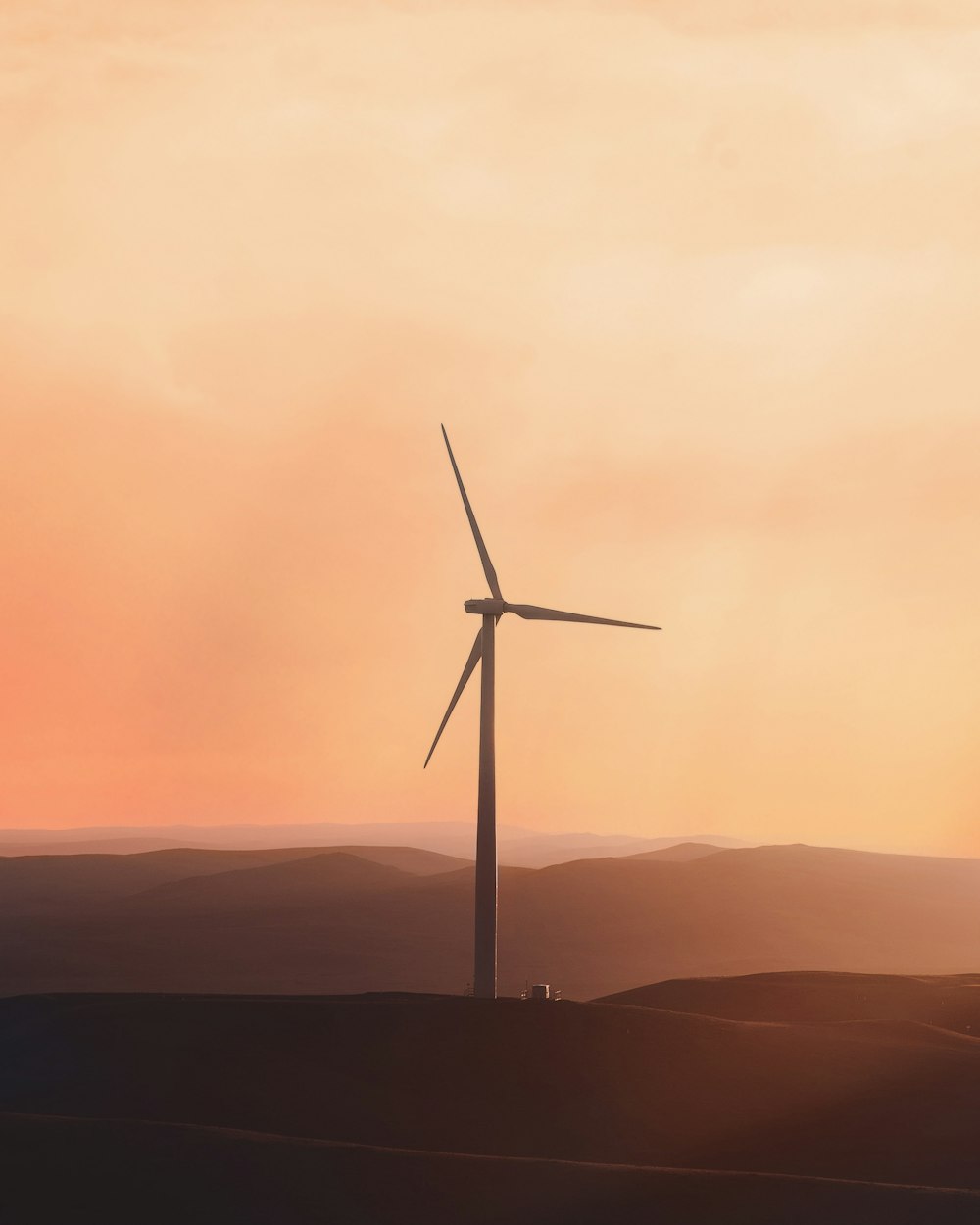 a wind turbine on a hill with a sunset in the background
