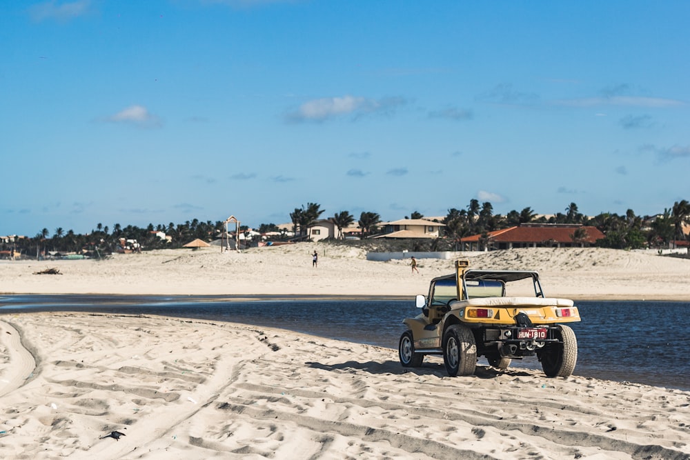 a jeep driving down a sandy beach next to a body of water