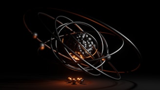 A dark, abstract, and futuristic representation of an atom, featuring a cluster of metallic spheres at the center surrounded by orbiting rings. The orange and black lighting adds a dramatic effect, emphasizing the spherical forms and giving a sense of depth.