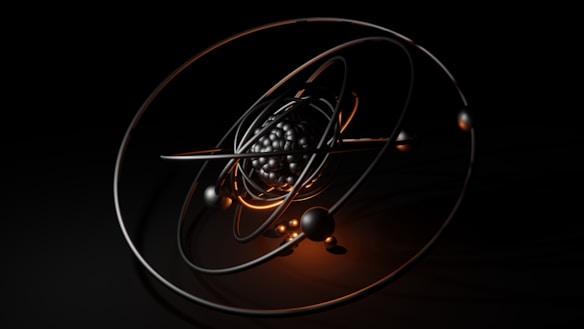 A 3D model of an atom with metallic and glossy elliptical rings surrounding a cluster of black and reflective spheres at the center, set against a dark background. Warm orange highlights accentuate the structure and add contrast to the composition.