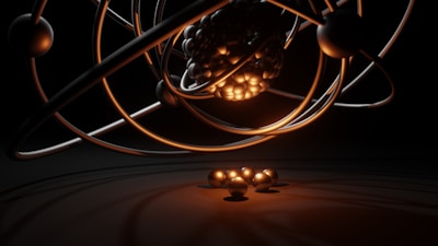 A 3D representation of an atomic structure with orbiting electrons. The nucleus is composed of tightly packed spheres and surrounded by several rings with individual spheres representing electrons. A warm glow illuminates the nucleus, casting shadows and reflections.