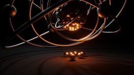 A 3D representation of an atomic structure with orbiting electrons. The nucleus is composed of tightly packed spheres and surrounded by several rings with individual spheres representing electrons. A warm glow illuminates the nucleus, casting shadows and reflections.