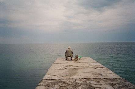 a man sitting on a pier next to a dog