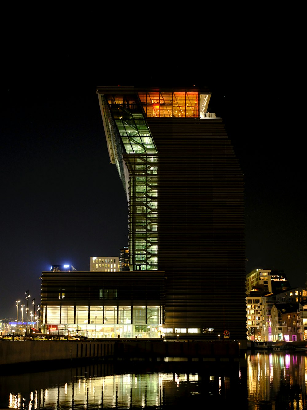 um edifício alto com um telhado iluminado ao lado de um corpo de água
