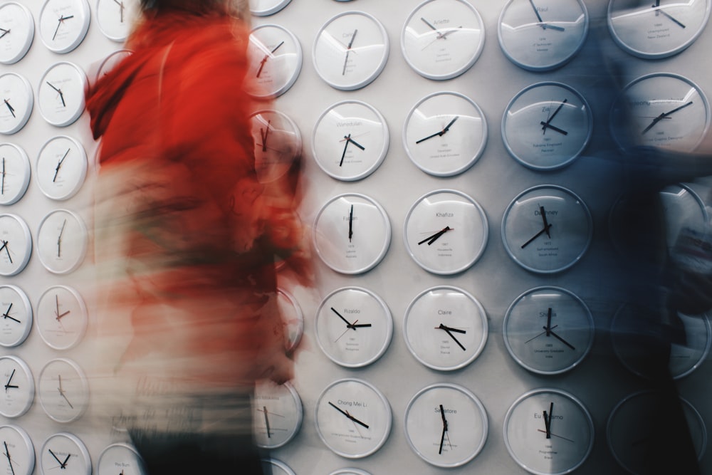 a woman standing in front of a wall covered in clocks