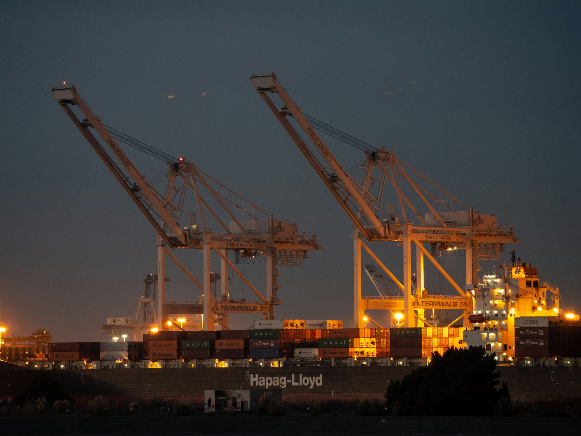 Large containers and cranes at a port at dusk, lit by yellow lights.