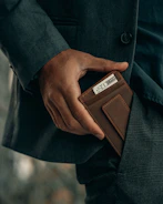 Lifestyle shot of a person slipping a stowly wallet into their jacket pocket on a city street.