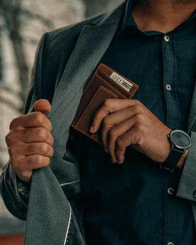 a black man holding a brown wallet that has $20 in it, and wearing a watch