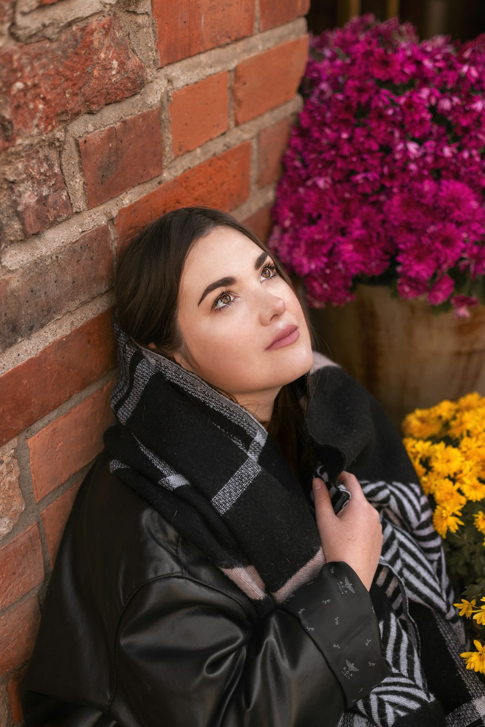a woman leaning against a brick wall next to flowers