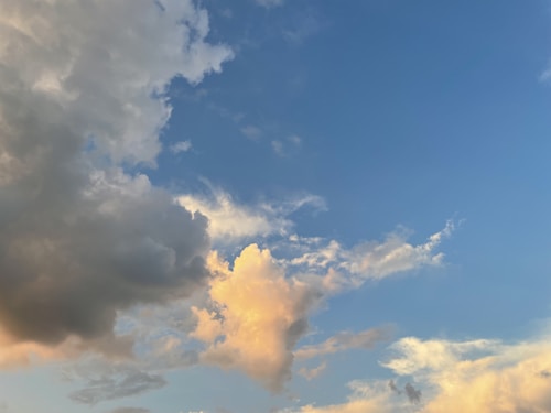 Various clouds fill the sky against a backdrop of blue. The clouds range from grey to white, with hints of orange and pink, suggesting the warm light of sunrise or sunset.