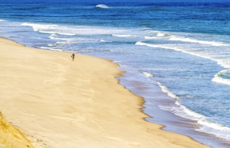 Golden sandy beach with gentle waves and a lone surfer catching a wave near the shore.
