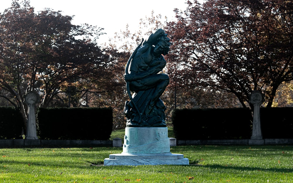 a statue of a man sitting on a pedestal in a park