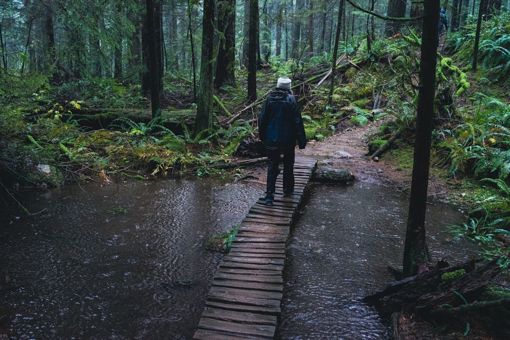 a man walking across a wooden bridge in the woods