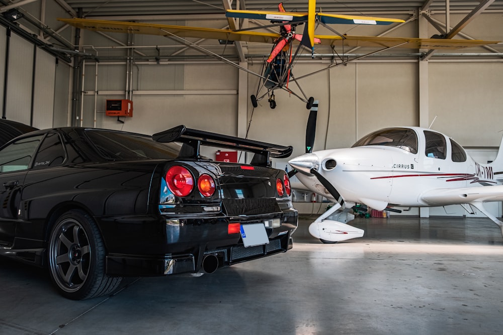 a black car parked in a garage next to a small plane