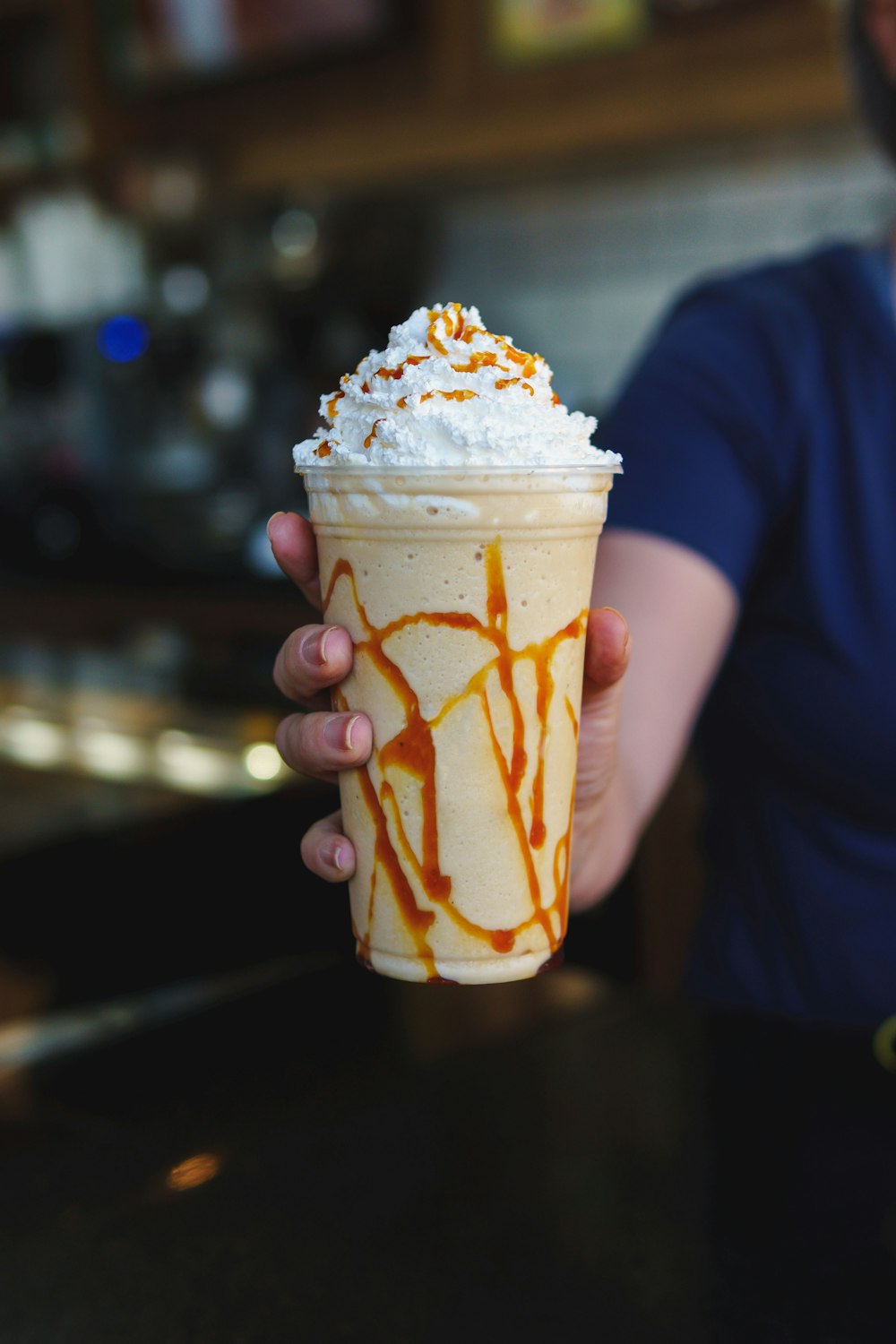a person holding a cup of ice cream with caramel drizzle