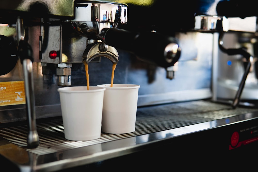 two cups of coffee being poured into a espresso machine