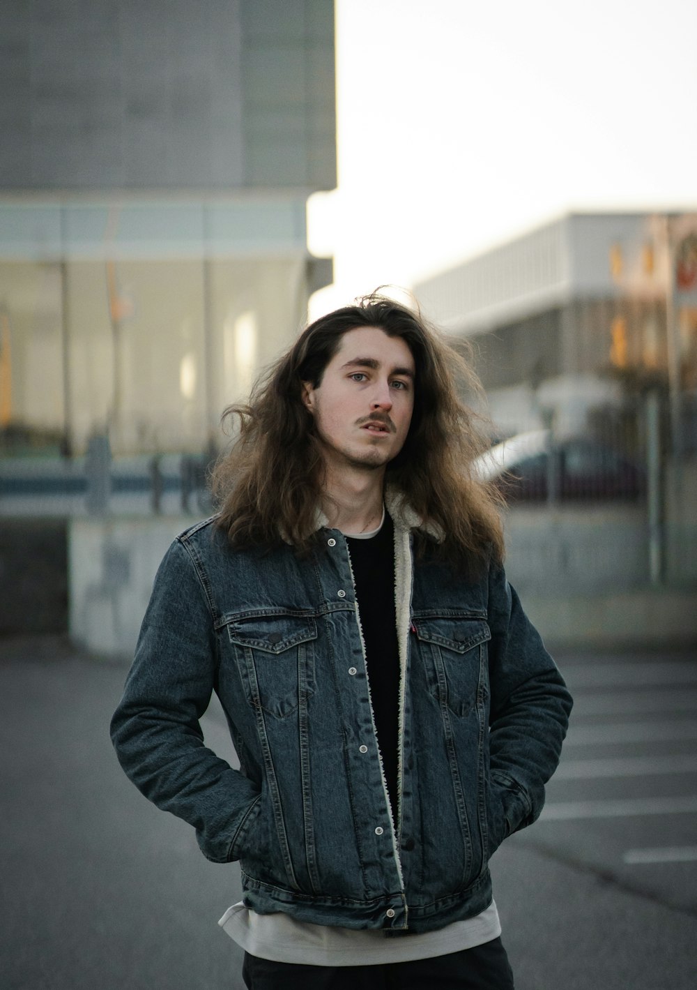 a man with long hair standing in a parking lot