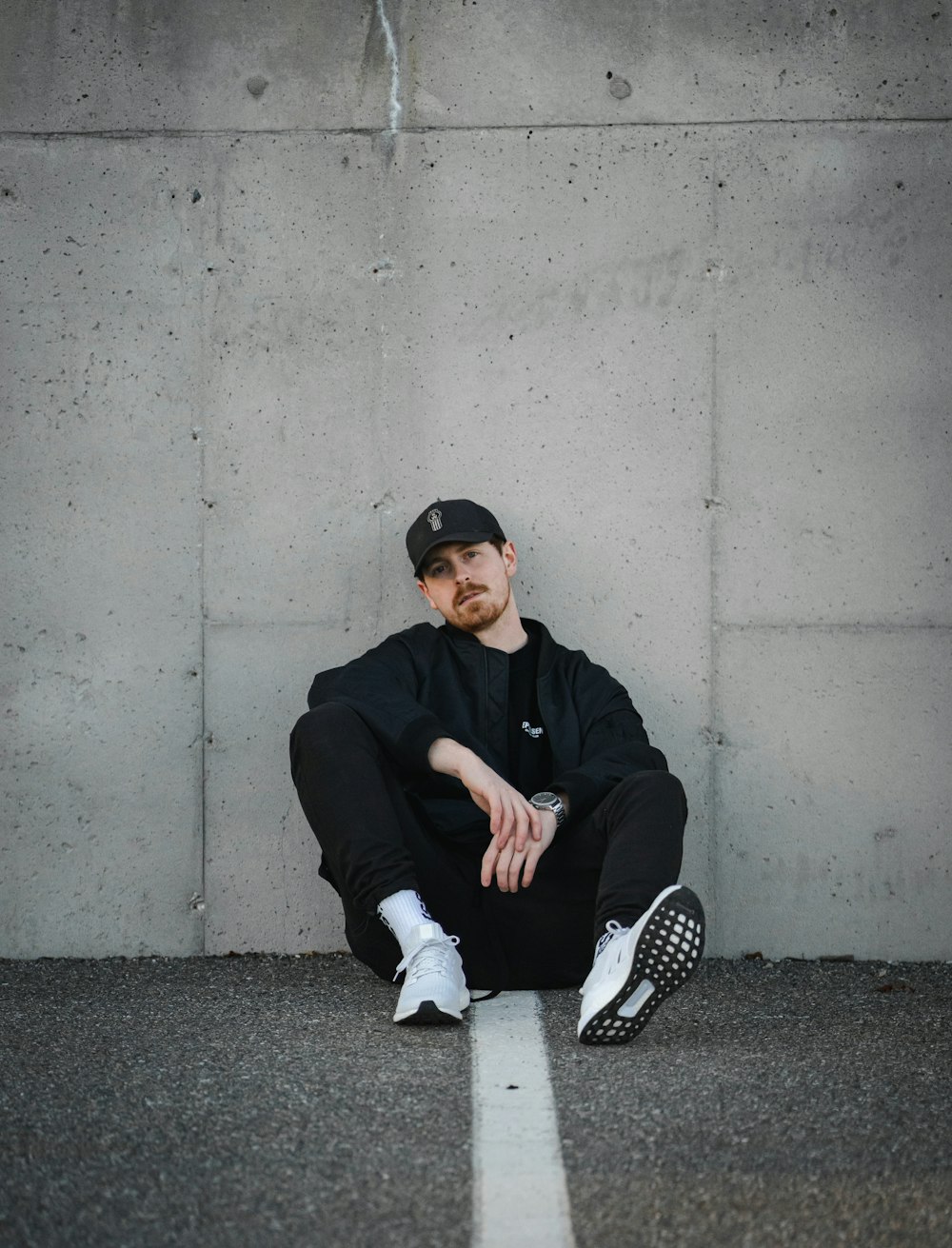 a man sitting on the ground in front of a concrete wall