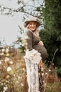 a pregnant woman in a hat poses in a field