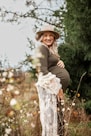 a pregnant woman in a hat poses in a field