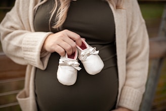 a pregnant woman holding a pair of baby shoes