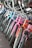 A row of colorful bicycles is lined up, showcasing a variety of designs and hues including blue, purple, pink, and orange. The bicycles are equipped with curved handlebars and some have wire baskets attached to the front. They are positioned on a brick-tiled surface near a glass window.